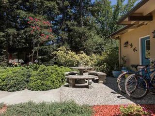 A tranquil garden sitting area with a stone table and benches, surrounded by lush plants and trees